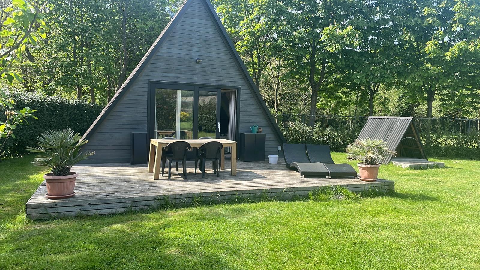 Modern A-frame poolhouse met donkere houten bekleding, grote glaspartijen en houten terras in groene tuinomgeving